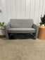 Gray outdoor sofa with a wooden armrest against a concrete wall.
