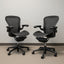 Two black office chairs with mesh backs against a white wall.